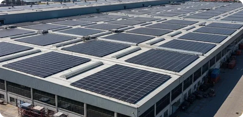 Aerial view of a massive warehouse roof completely covered in solar panels, with industrial buildings and roads in the background.
